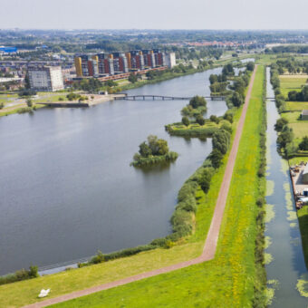 Luchtfoto van een rivier met dijk en ernaast een lager gelegen polder