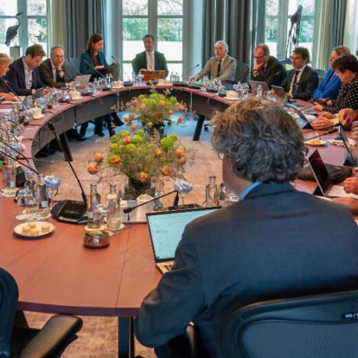 Bestuurlijkoverleg tussen ministerie, IPO, VNG en Unie van Waterschappen. De ruimte is klein en is een ovale tafel waar bestuurders zij aan zij aan zitten. Meindert Smallenbroek ziet men op de rug op de voorgrond van het beeld.