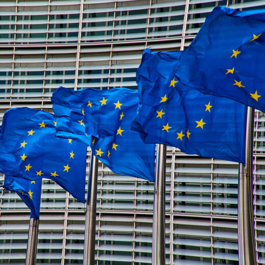 Vier blauwe vlaggen met gele sterren, de vlag van de Europese Unie, wapperen in de wind voor het gebouw van het Europees parlement in Brussel.