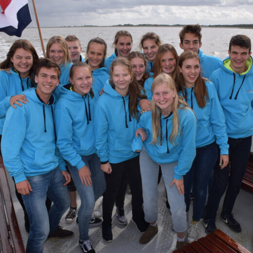 De jeugdwaterschappers van 2019 tijdens een werkbezoek op een boot. Alle jeugdwaterschappers dragen een blauwe trui.